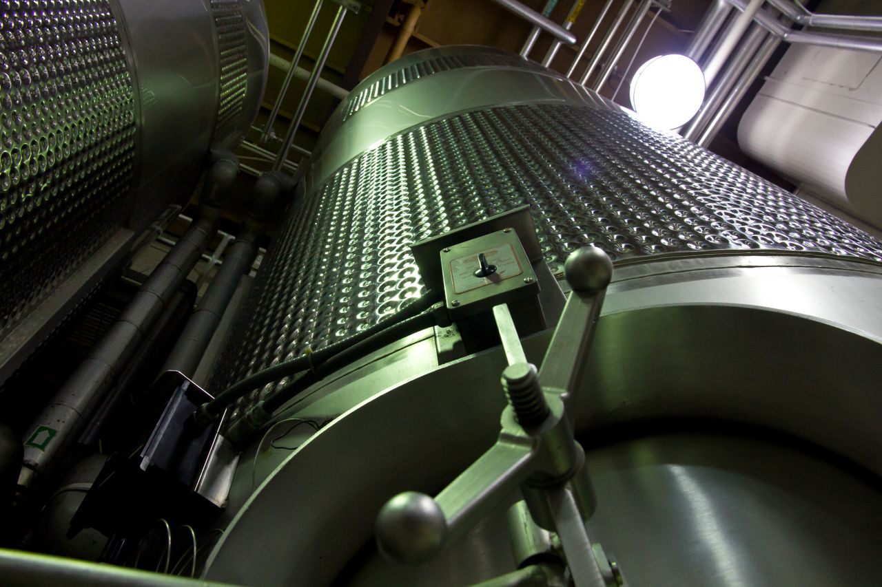About Low-angle shot of large stainless steel tanks inside a modern industrial facility.