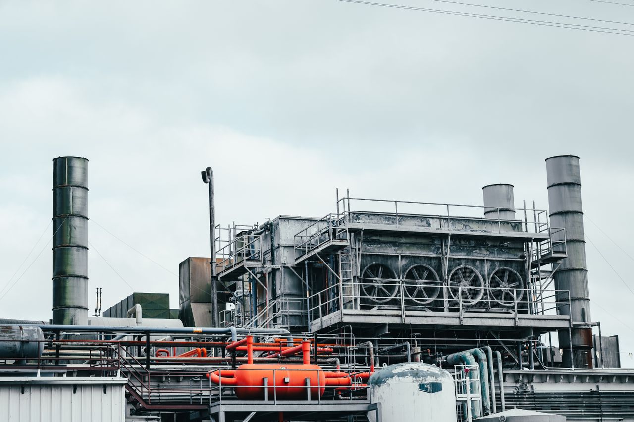 Services Industrial factory with metal pipes and special equipment surrounded with fences located against cloudy sky on street with power lines in town